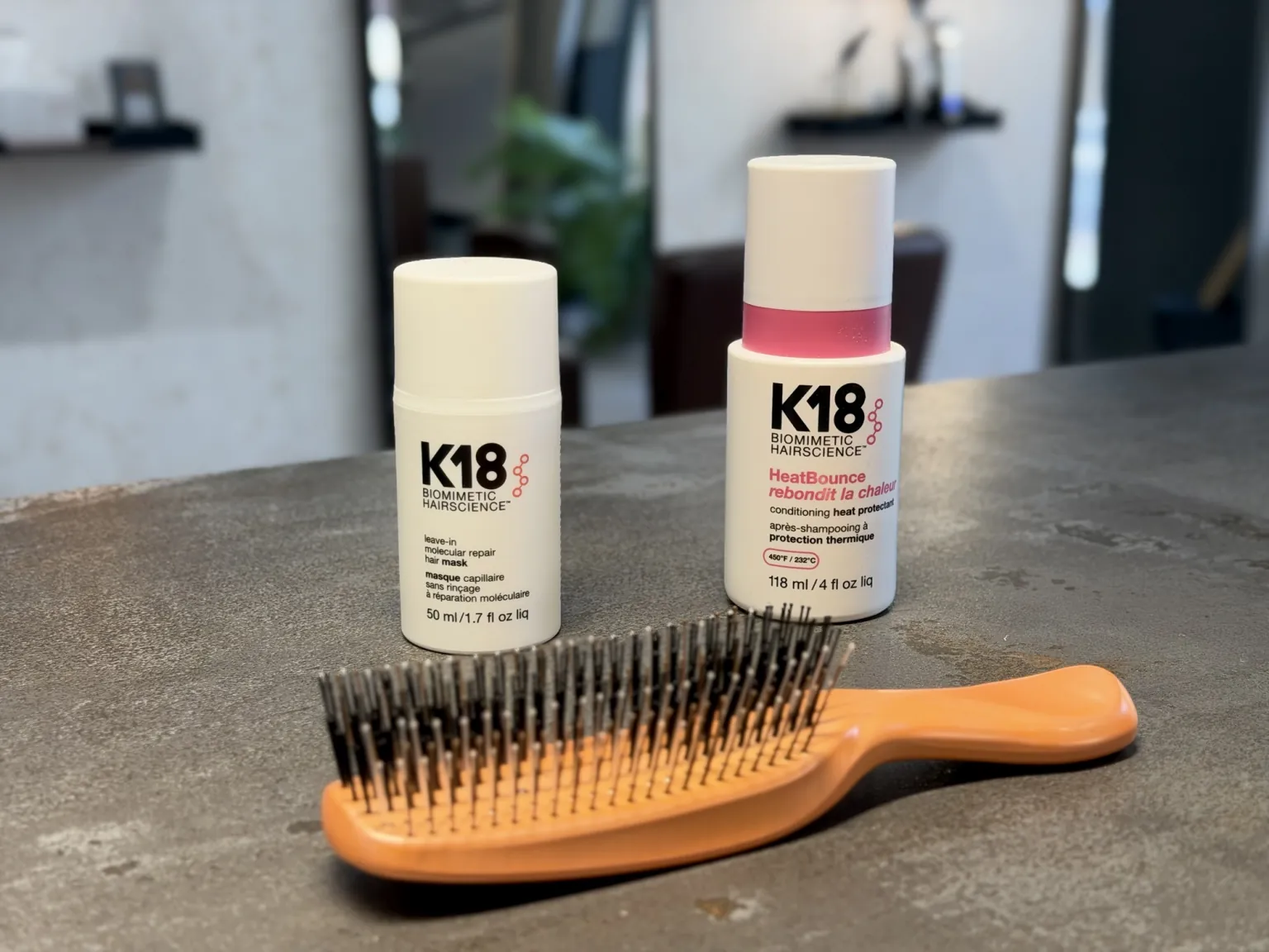K18 leave-in repair mask and HeatBounce heat protectant next to a hairbrush at Milanocenter Estilismo, Elche